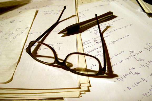 Reading glasses and pen placed on top of a stack of paper assessments